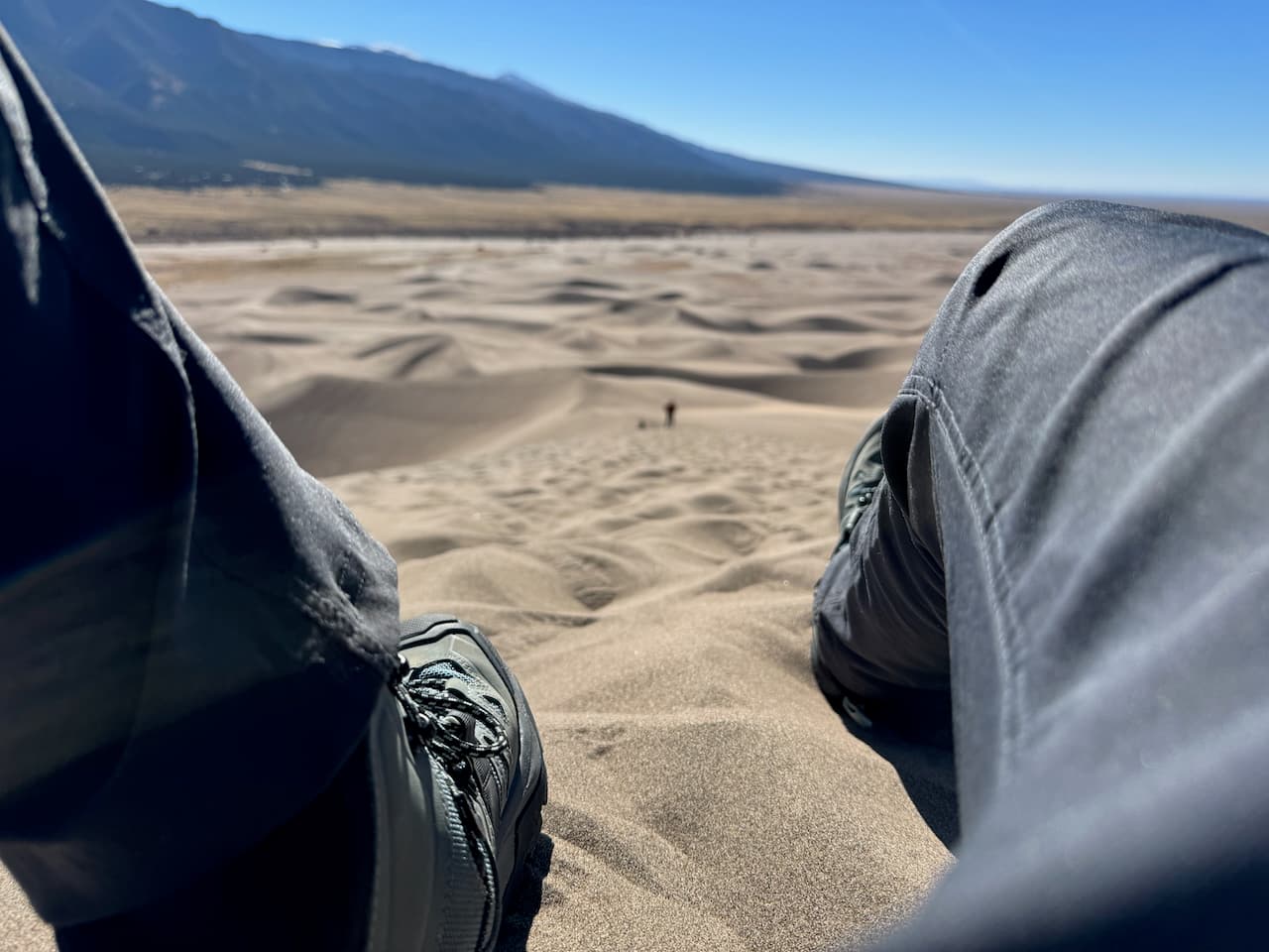 Sitting down for a break climbing the dune field, taking a shot down at the climb, legs and boots in view