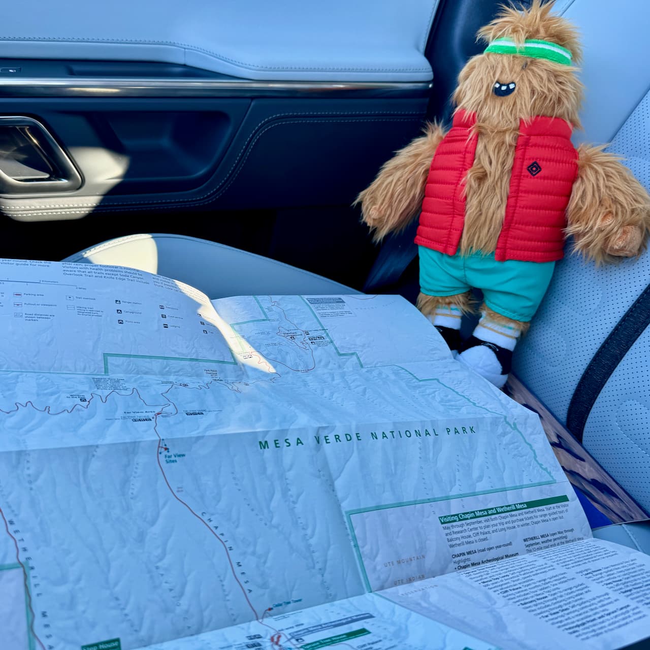 Gear Guard stuffie sitting on the Rivian R1S's passenger seat, looking over a map of Mesa Verde National Park