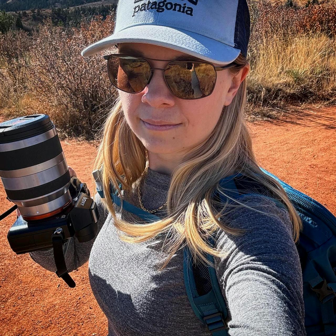 Selfie of Jade Pennig, wearing a hat and sunglasses, holding a Sony A7R camera