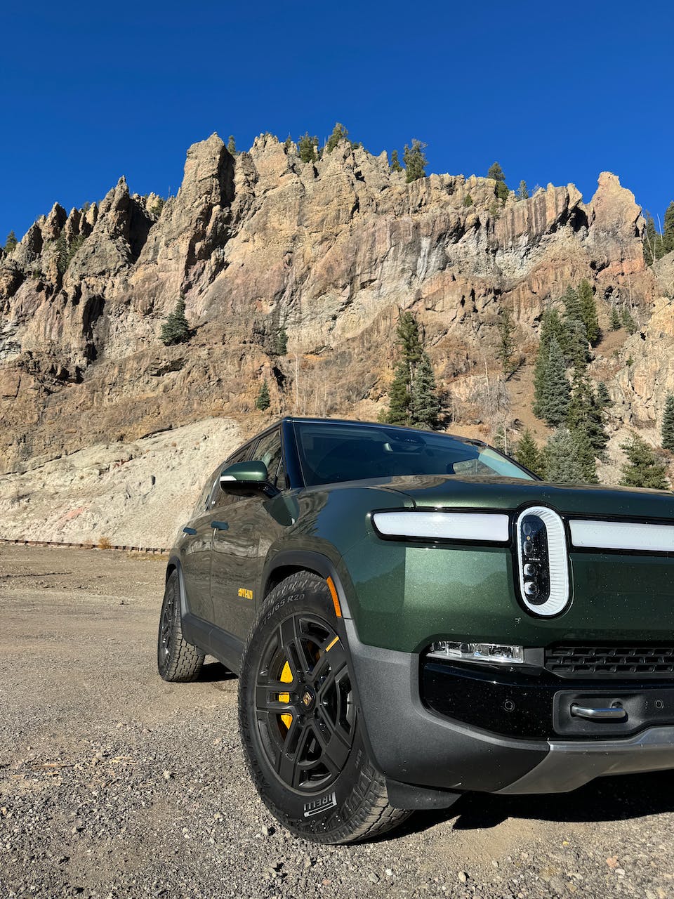 A side shot of a green Rivian R1S on the side of the highway in southern Colorado