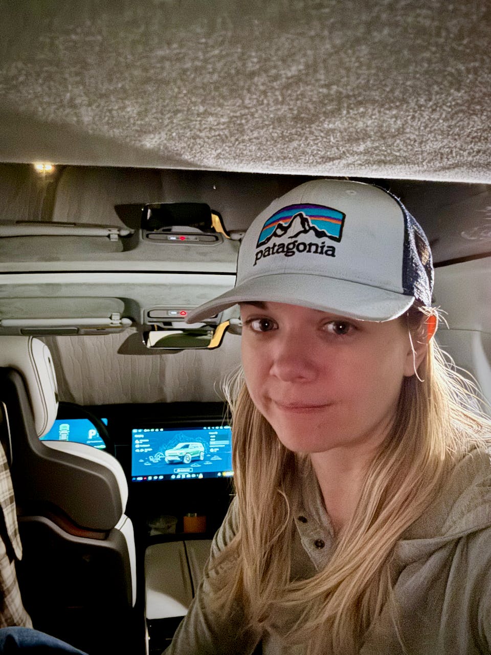 Selfie of Jade Pennig in the back of her Rivian R1S, camera facing the dash, which shows camping mode controls
