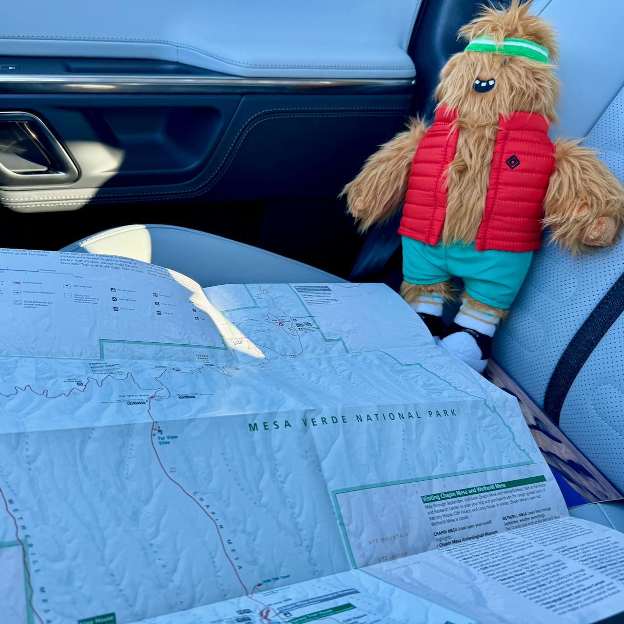Gear Guard stuffie sitting on the Rivian R1S's passenger seat, looking over a map of Mesa Verde National Park